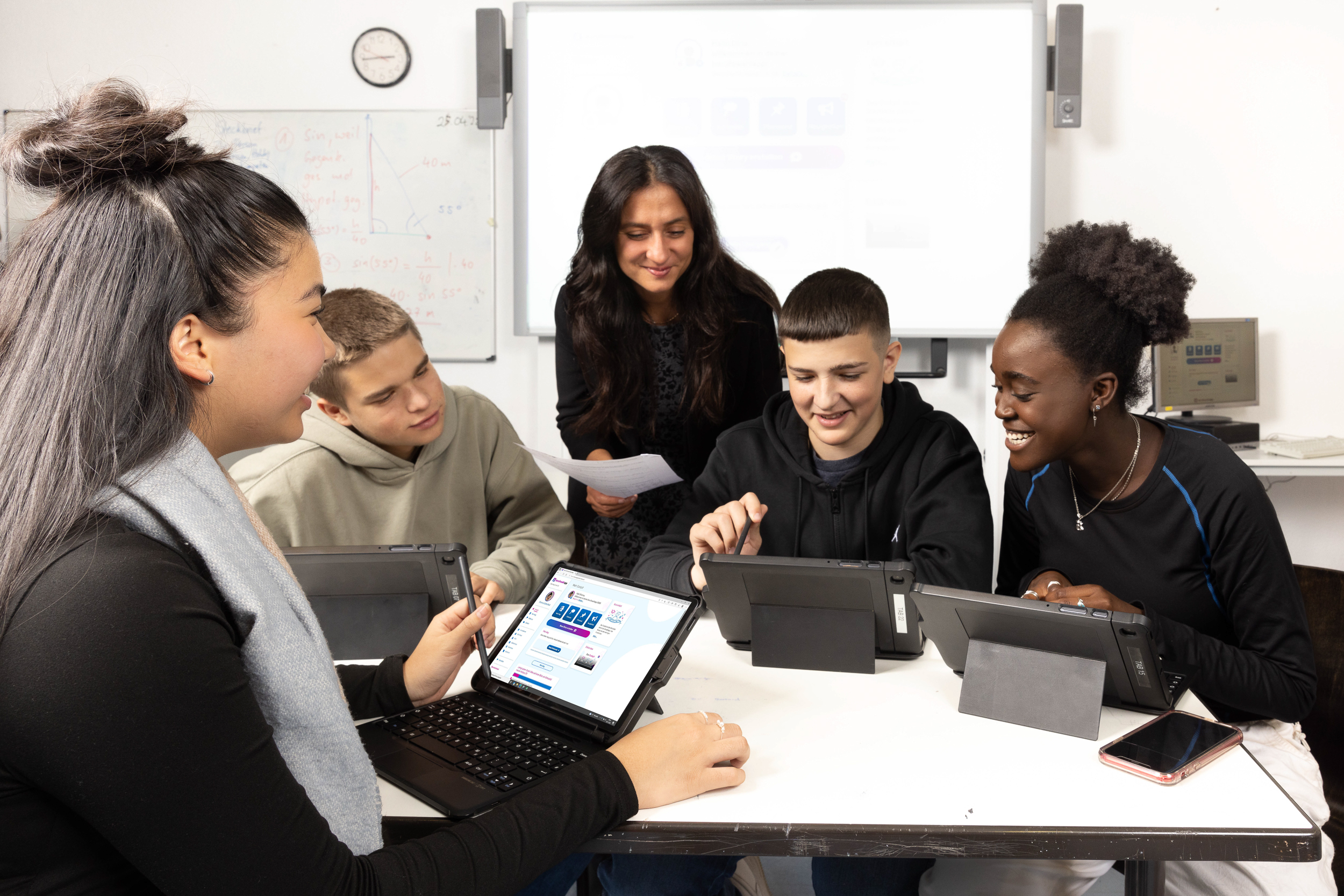 Vier jugendliche Schülerinnen und Schüler und eine weibliche Lehrkraft sitzen an einem Tisch und arbeiten mit Tablet-Computern in der berufswahlapp.