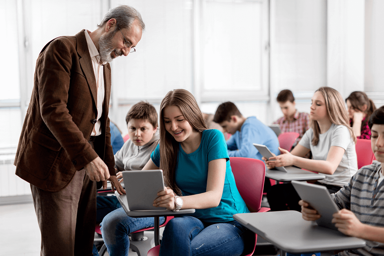 Lehrer schaut in Schulklasse mit Schülerin gemeinsam auf ein Tablet
