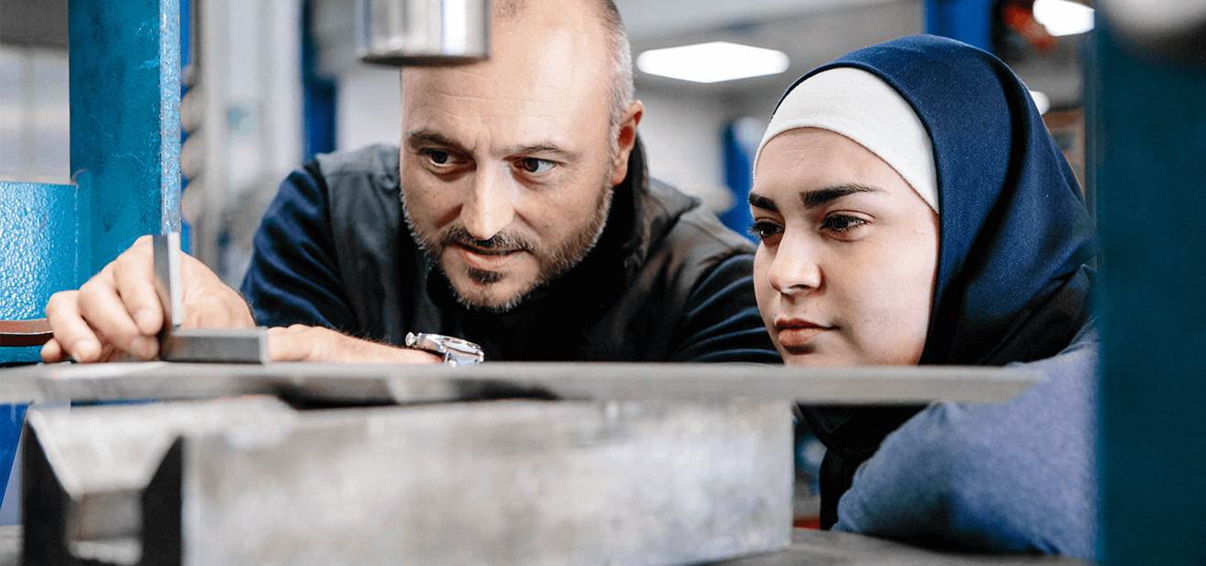 Ausbilder untersucht mit Schülerin Metallteile in Werkstatt